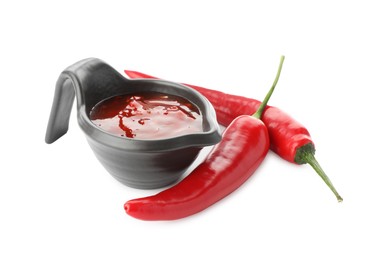 Photo of Hot chili sauce in gravy boat and peppers isolated on white