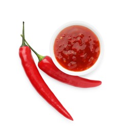 Photo of Hot chili sauce in bowl and peppers isolated on white, top view