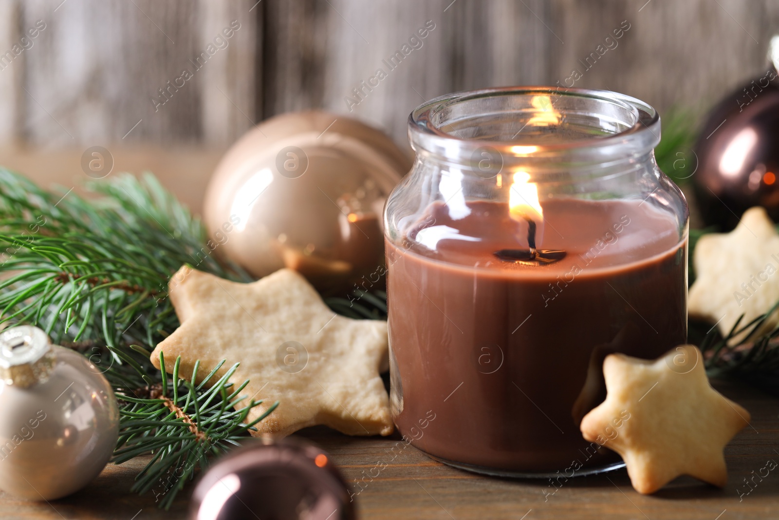 Photo of Burning candle, baubles, cookies and fir branches on wooden table, closeup. Christmas atmosphere