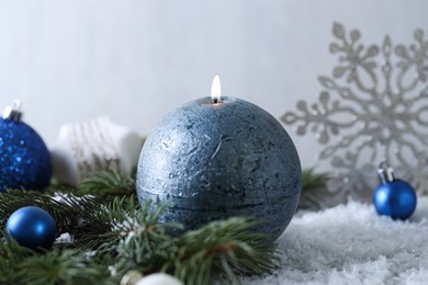 Photo of Burning candle, baubles and fir branches on artificial snow, closeup. Christmas atmosphere