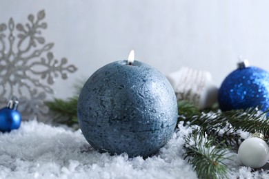 Photo of Burning candle, baubles and fir branches on artificial snow, closeup. Christmas atmosphere