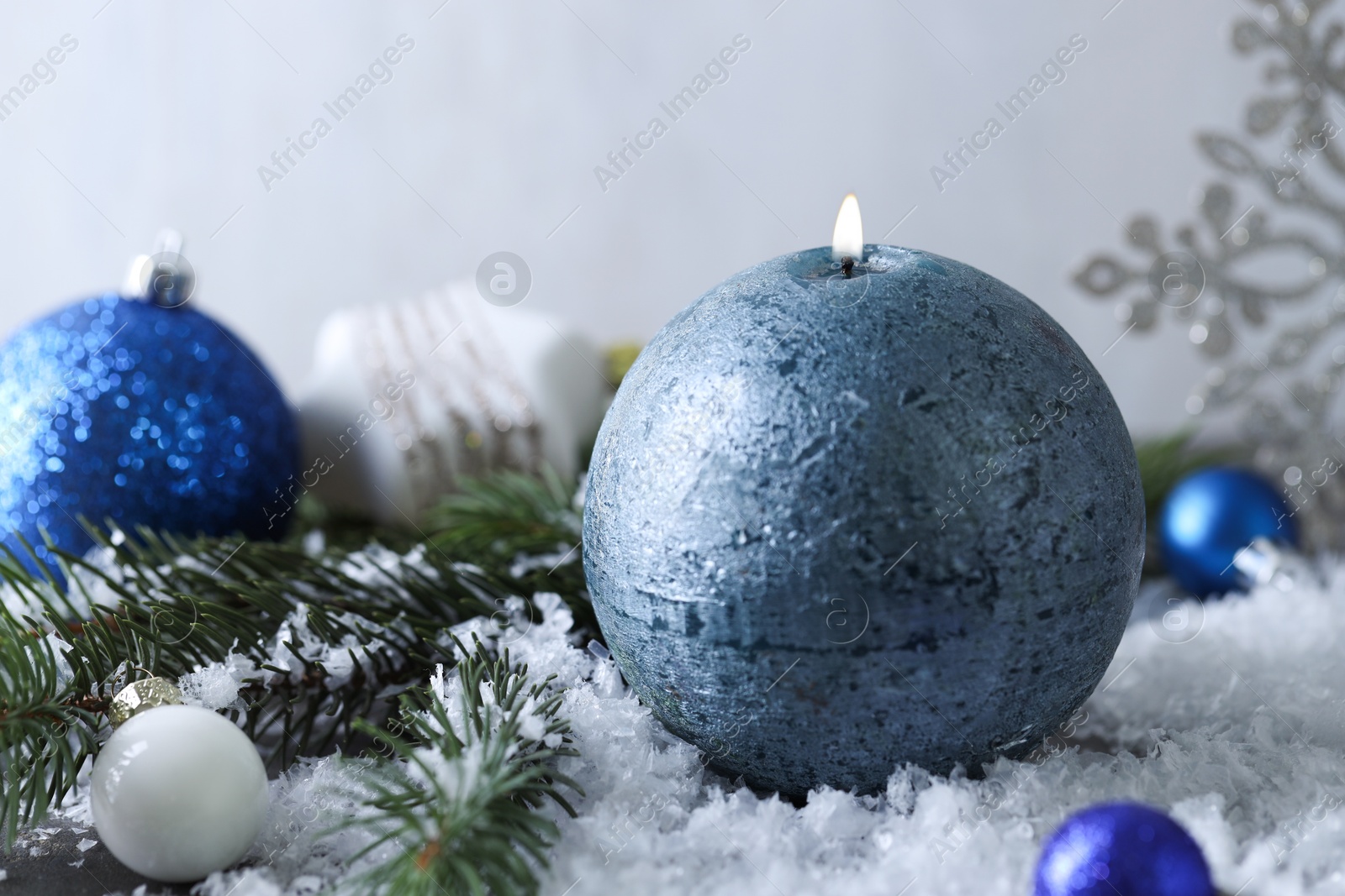 Photo of Burning candle, baubles and fir branches on artificial snow, closeup. Christmas atmosphere