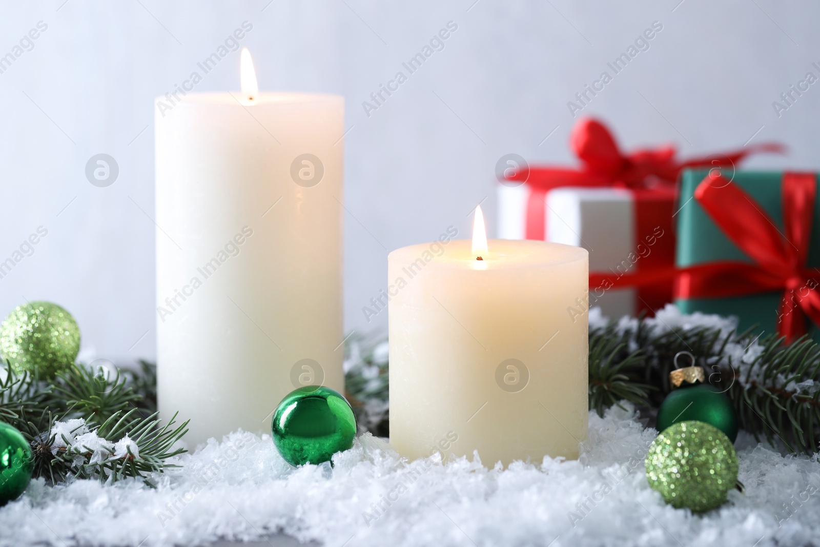 Photo of Burning candles, baubles and fir branches on artificial snow, closeup. Christmas atmosphere