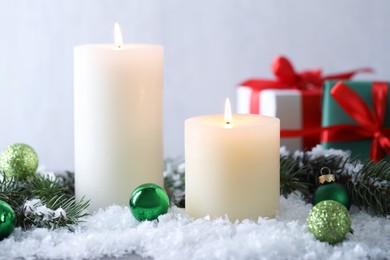 Photo of Burning candles, baubles and fir branches on artificial snow, closeup. Christmas atmosphere