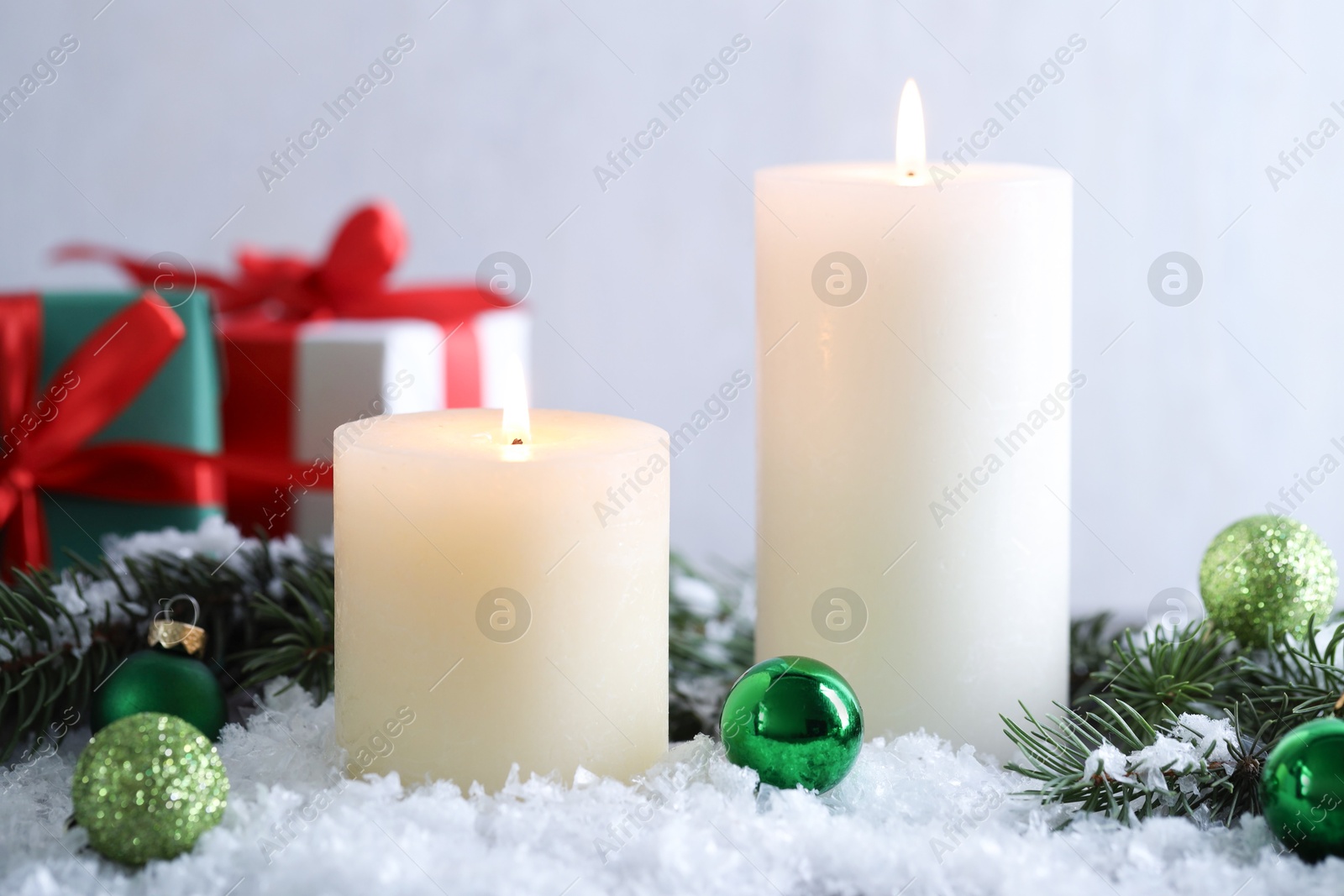 Photo of Burning candles, baubles and fir branches on artificial snow, closeup. Christmas atmosphere