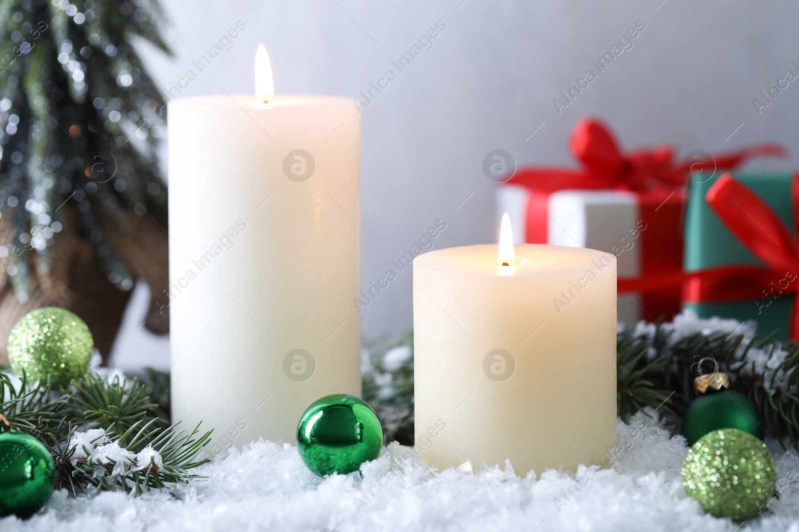 Photo of Burning candles, baubles and fir branches on artificial snow, closeup. Christmas atmosphere