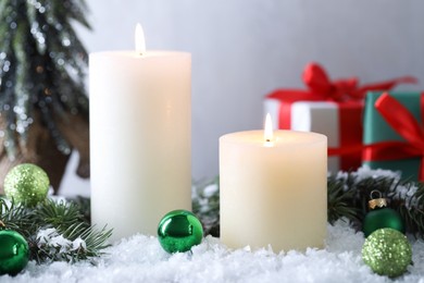 Photo of Burning candles, baubles and fir branches on artificial snow, closeup. Christmas atmosphere