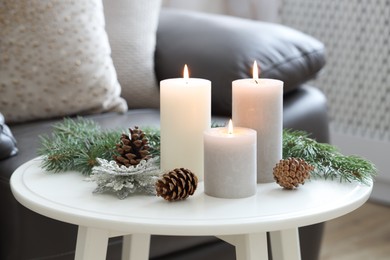 Photo of Burning candles, fir branches and other Christmas decor on coffee table indoors