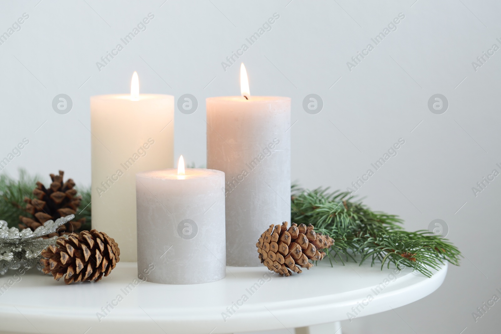 Photo of Burning candles and fir branches on coffee table near light wall, space for text. Christmas atmosphere