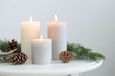 Photo of Burning candles and fir branches on coffee table near light wall, space for text. Christmas atmosphere