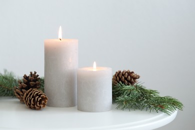 Photo of Burning candles and fir branches on coffee table near light wall, space for text. Christmas atmosphere