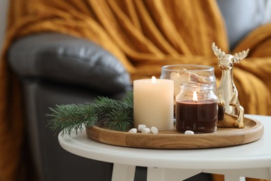 Photo of Burning candles, fir branches and decorative deer on coffee table indoors, space for text. Christmas atmosphere