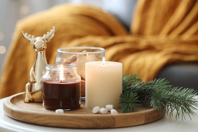 Photo of Burning candles, fir branches and decorative deer on coffee table indoors. Christmas atmosphere