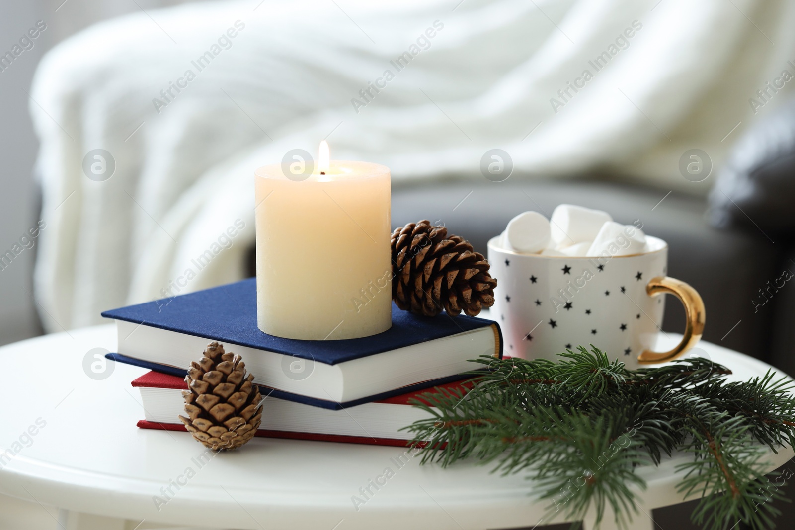 Photo of Burning candle, books, fir branches and cones on coffee table indoors. Christmas atmosphere