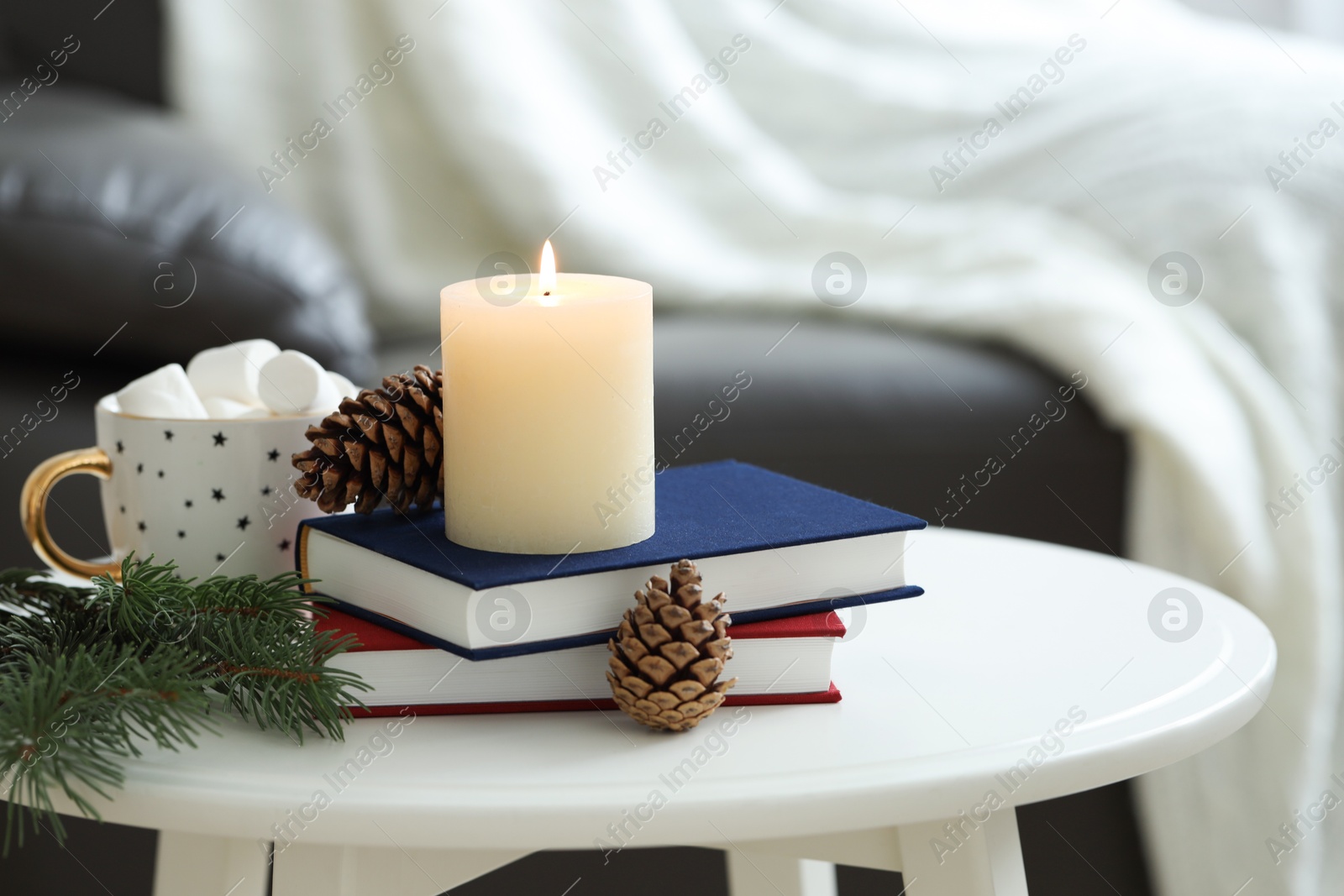 Photo of Burning candle, books, fir branches and cones on coffee table indoors. Christmas atmosphere