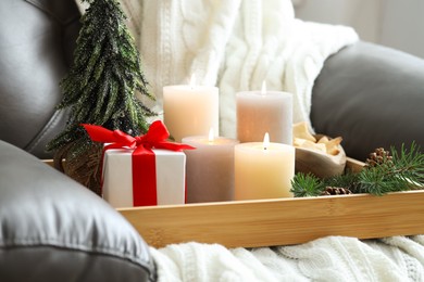 Photo of Tray with burning candles and Christmas decor on armchair