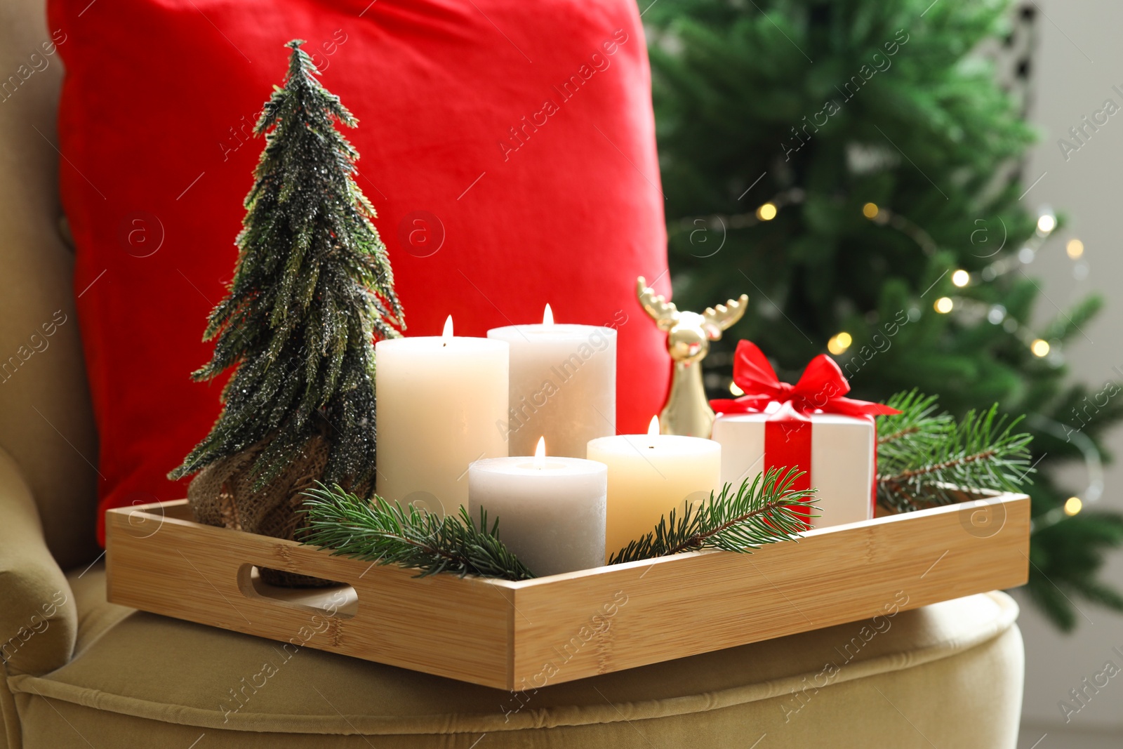 Photo of Tray with burning candles and Christmas decor on armchair indoors