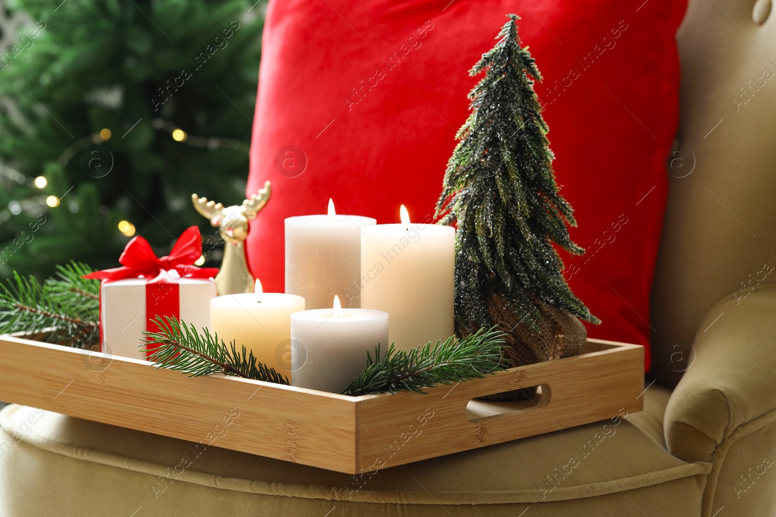 Photo of Tray with burning candles and Christmas decor on armchair indoors