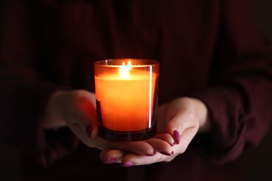 Photo of Woman with burning candle in darkness, closeup