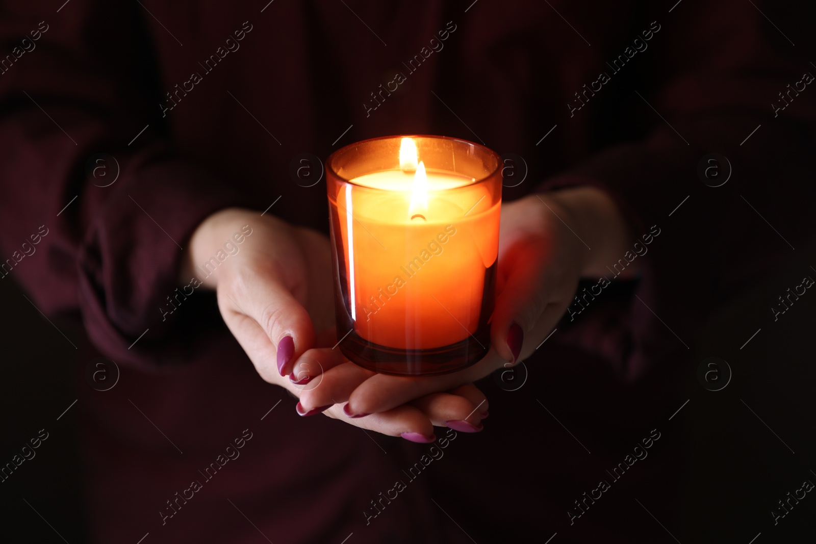 Photo of Woman with burning candle in darkness, closeup