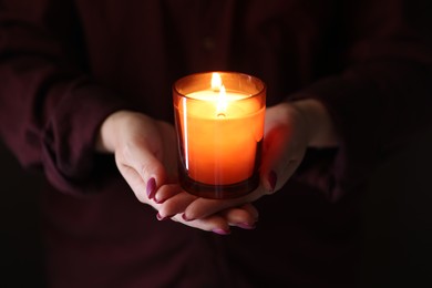 Photo of Woman with burning candle in darkness, closeup