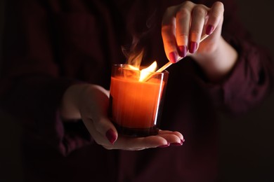 Photo of Woman lighting candle with match in darkness, closeup