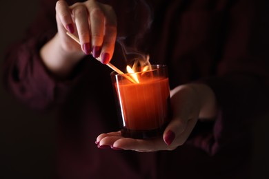 Photo of Woman lighting candle with match in darkness, closeup