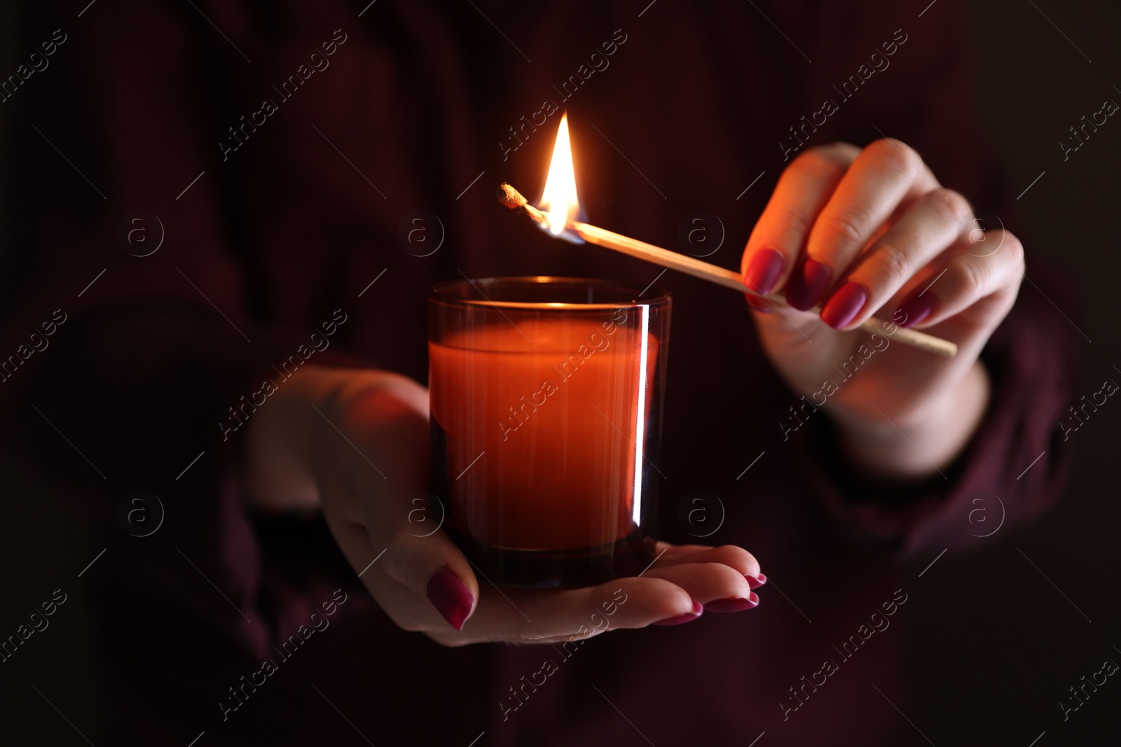 Photo of Woman lighting candle with match in darkness, closeup