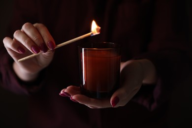 Photo of Woman lighting candle with match in darkness, closeup