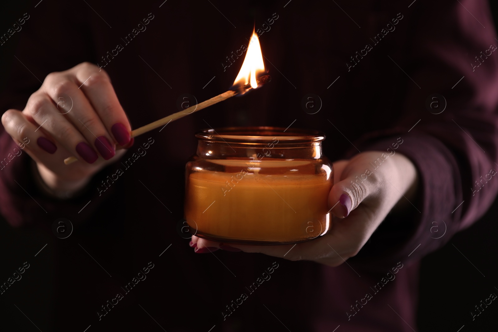 Photo of Woman lighting candle with match in darkness, closeup