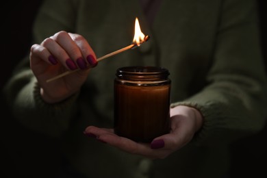 Photo of Woman lighting candle with match in darkness, closeup