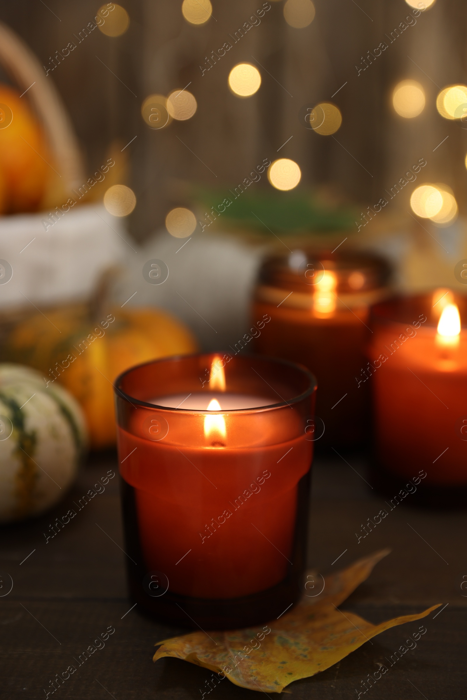 Photo of Burning candles and autumn decor on wooden table, closeup