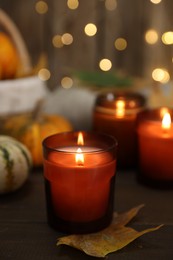 Photo of Burning candles and autumn decor on wooden table, closeup