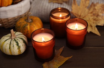 Photo of Burning candles and autumn decor on wooden table, closeup