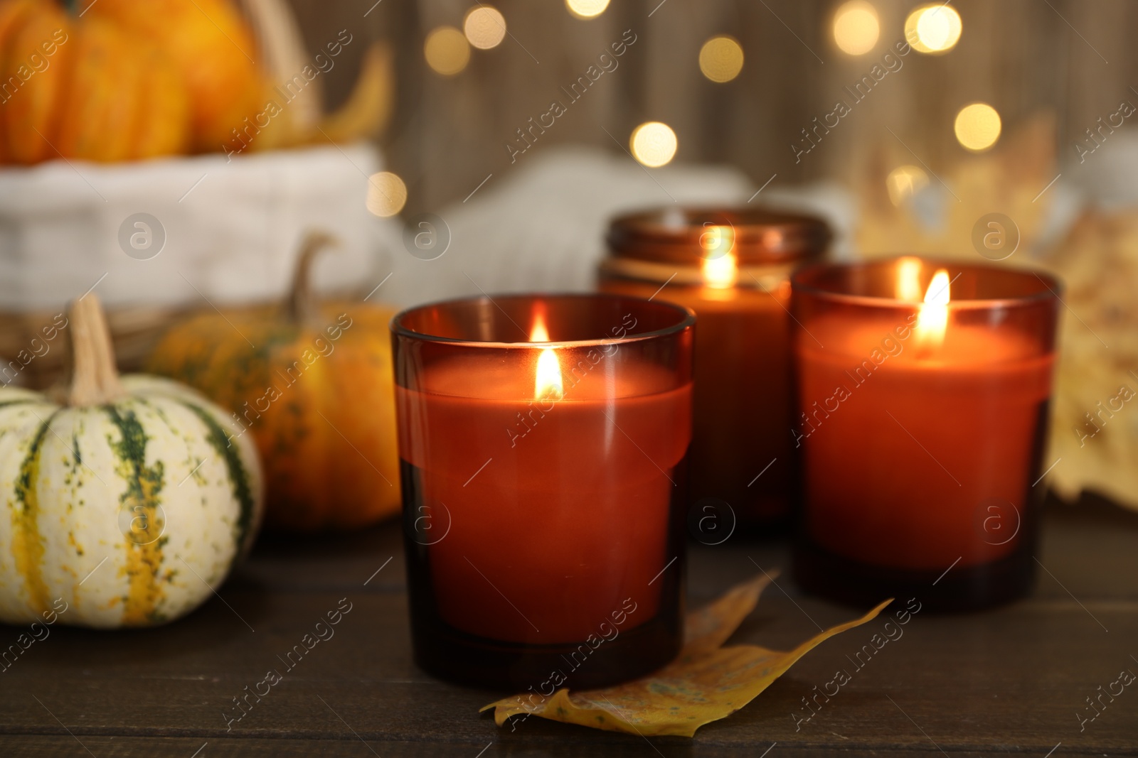 Photo of Burning candles and autumn decor on wooden table, closeup