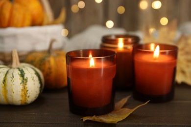 Photo of Burning candles and autumn decor on wooden table, closeup