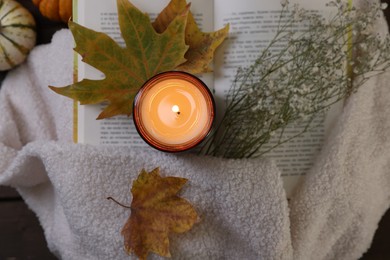 Photo of Burning candle, open book, sweater and autumn decor on table, top view