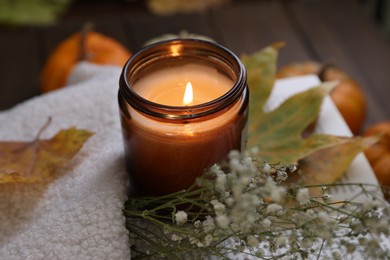 Burning candle, sweater and autumn decor on table, closeup