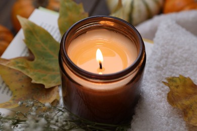 Photo of Burning candle, sweater and autumn decor on table, closeup