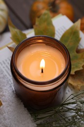 Photo of Burning candle, open book, sweater and autumn decor on table, closeup