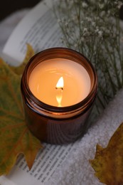 Photo of Burning candle, open book, sweater and autumn decor on table, closeup