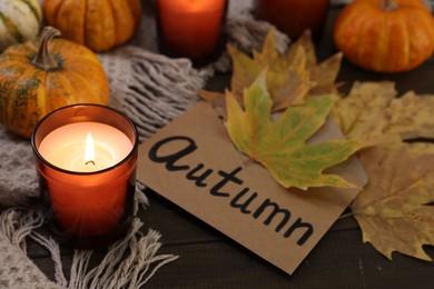 Photo of Envelope with word Autumn, burning candle, dry leaves and pumpkins on wooden table, closeup