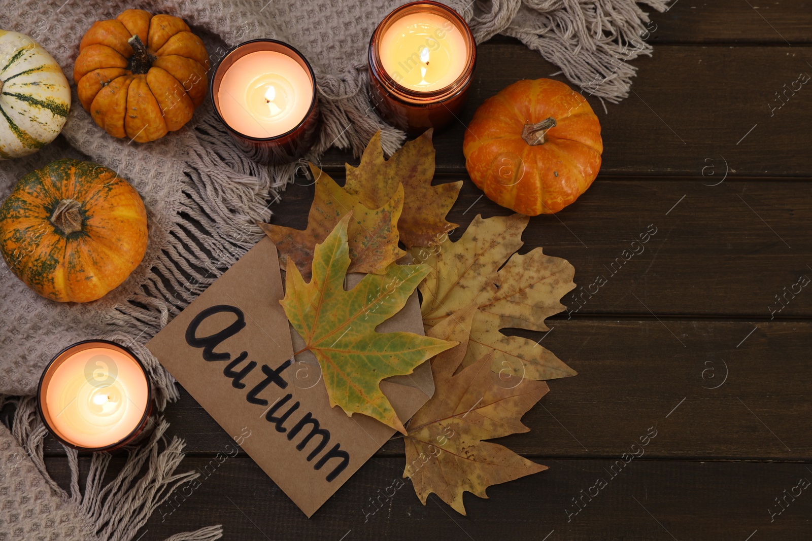 Photo of Envelope with word Autumn, burning candles, dry leaves and pumpkins on wooden table, top view