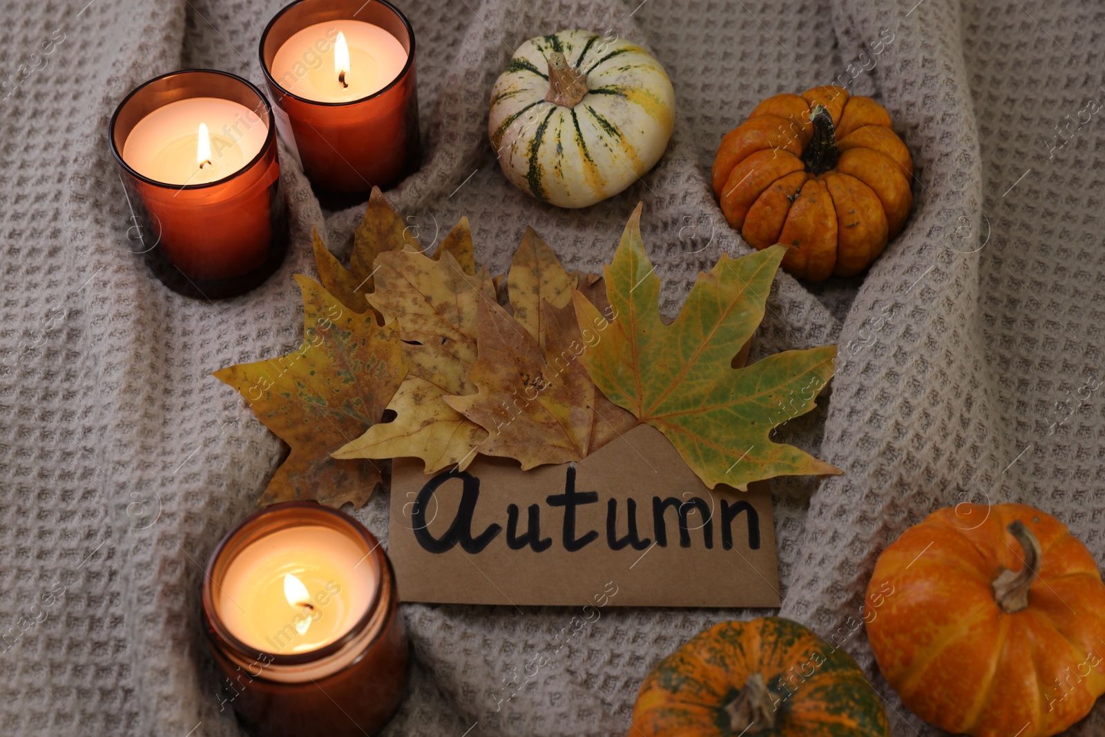 Photo of Envelope with word Autumn, burning candles, dry leaves and pumpkins on blanket, above view