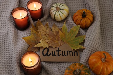 Photo of Envelope with word Autumn, burning candles, dry leaves and pumpkins on blanket, above view