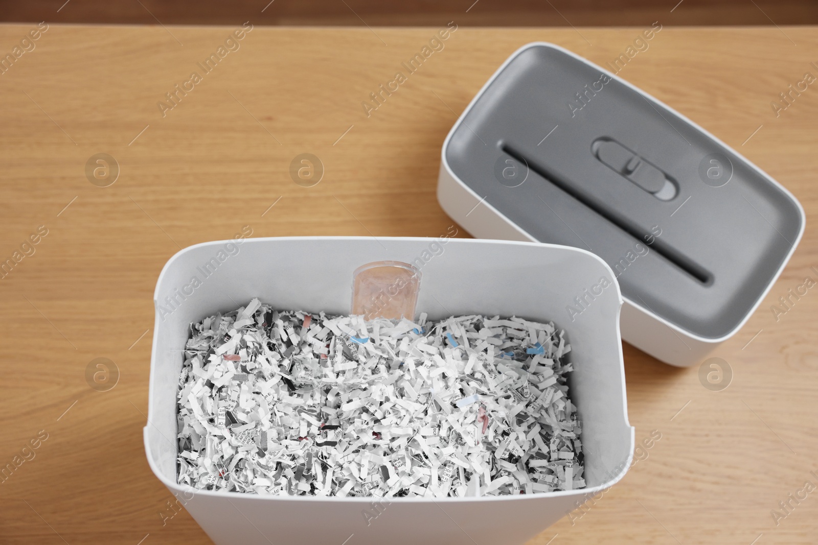 Photo of Shredder and basket with paper strips on wooden table, above view