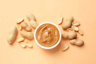 Photo of Tasty peanut butter in bowl and groundnuts on beige background, flat lay