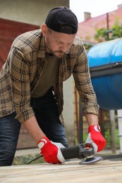 Man polishing wooden planks with angle grinder outdoors