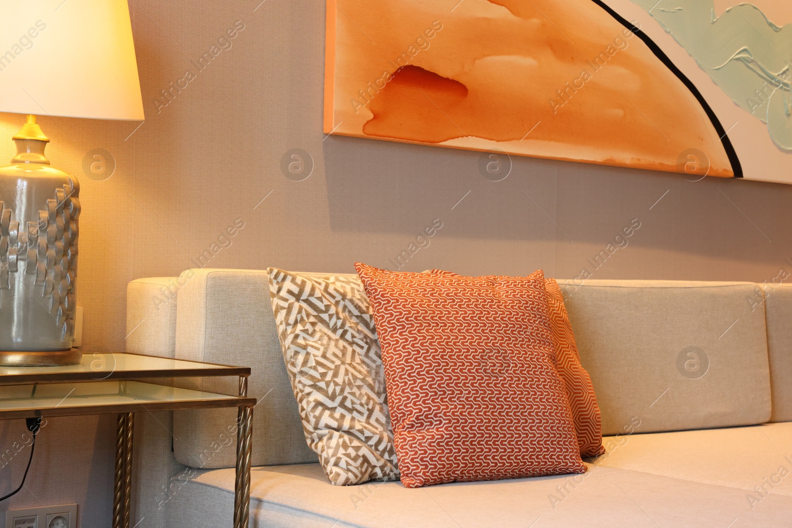 Photo of Comfortable sofa with cushions and lamp on side table in room