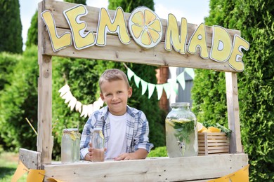 Photo of Cute little boy with refreshing drink at lemonade stand in park